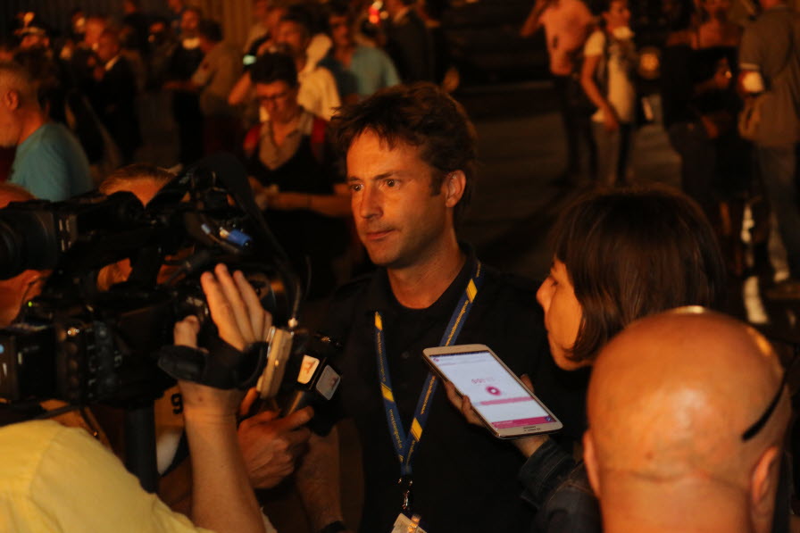 Mörkhårig man i folkhav med journalister vid en pressträff utomlands i kvällsljus. 